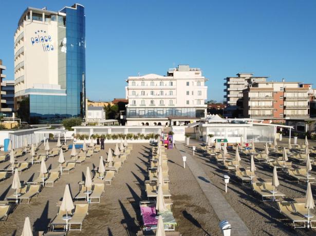 Strand mit geschlossenen Sonnenschirmen, modernes Hotel im Hintergrund.